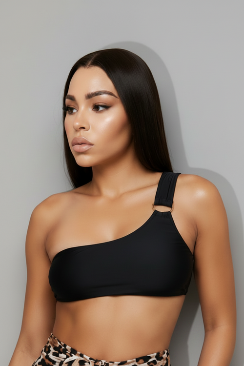 Model wearing a black one-shoulder bikini top paired. The look is completed with rectangular tortoise sunglasses against a light gray studio background.